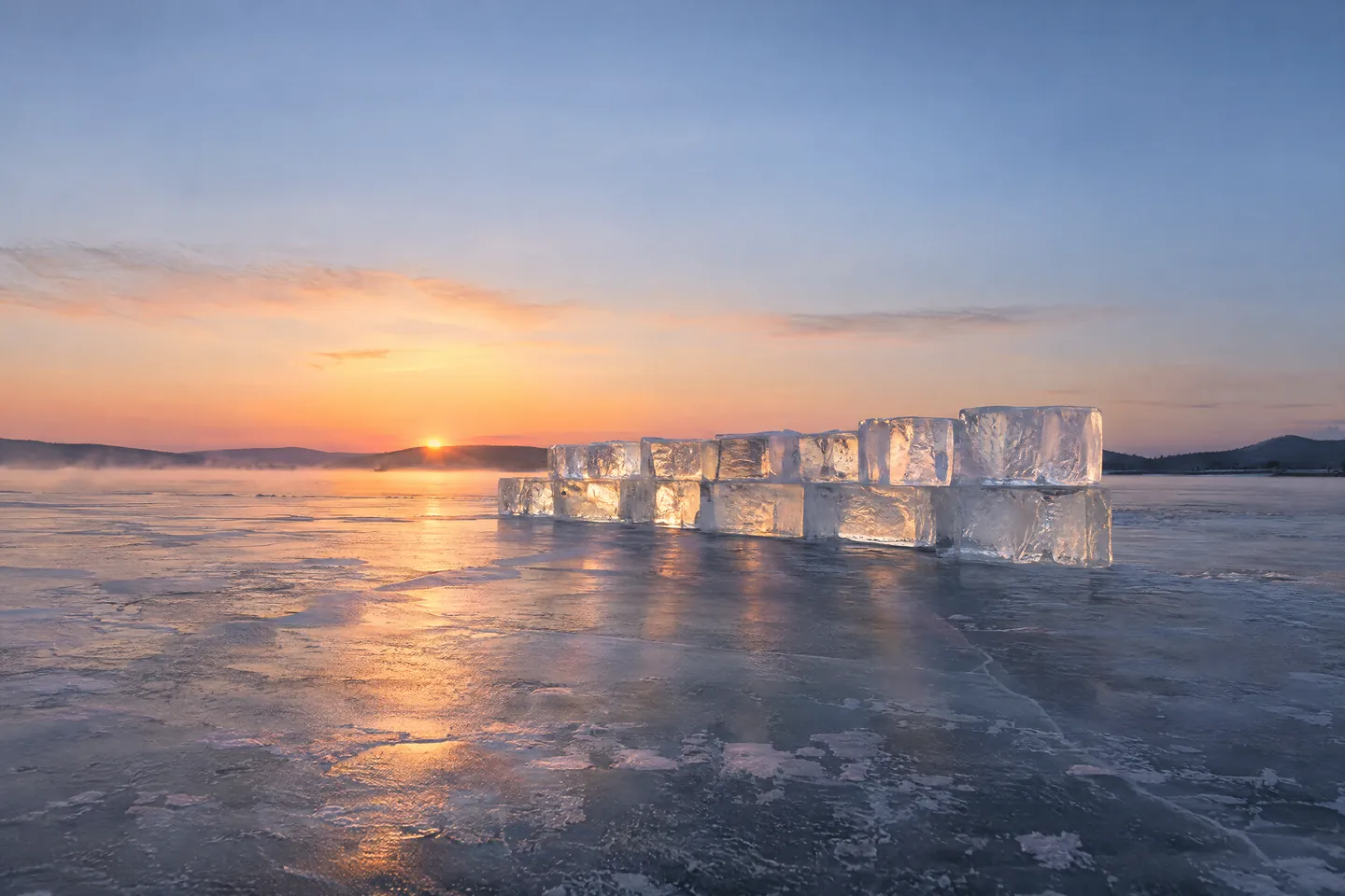 Hand-cut blocks of clear ice stacked on a frozen lake, lit through by a low sunrise